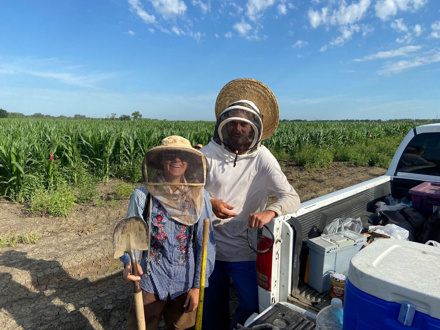 Two crew members in sun hats and veils beside the water truck